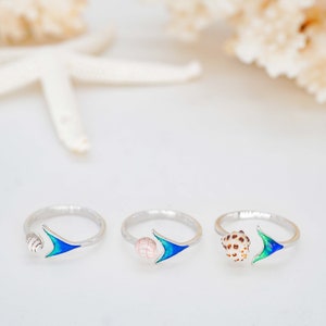 May include: Three silver rings with a blue and green enamel arrow design. Each ring features a different seashell on the side.