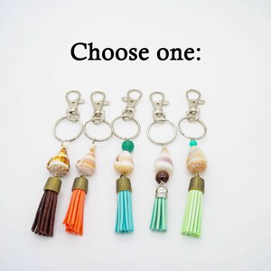 May include: Five keychains with different colored tassels and seashell charms. The tassels are brown, orange, turquoise, green, and light green. The charms are all seashells with a brown, white, and pink color scheme.  Choose one: