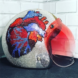 May include: A motorcycle helmet with a clear visor and a red, blue, and white heart design covered in rhinestones.