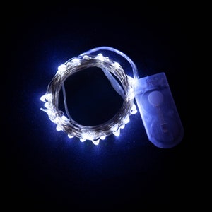 May include: A string of white LED fairy lights with a battery pack. The lights are coiled in a circle and are on a dark blue background.