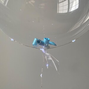 K&ouml;nnte beinhalten: Ein transparenter Ballon mit einem blauen Band und wei&szlig;en Lichterketten.