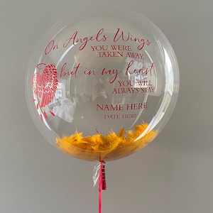 K&ouml;nnte beinhalten: Ein transparenter Ballon mit gelben Federn im Inneren. Der Ballon tr&auml;gt eine rote Aufschrift mit dem Text "On Angels Wings You Were Taken Away, But In My Heart You Will Always Stay. Name Here Date Here."