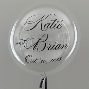 May include: Clear balloon with black lettering that reads "Katie and Brian Oct. 30, 2023".