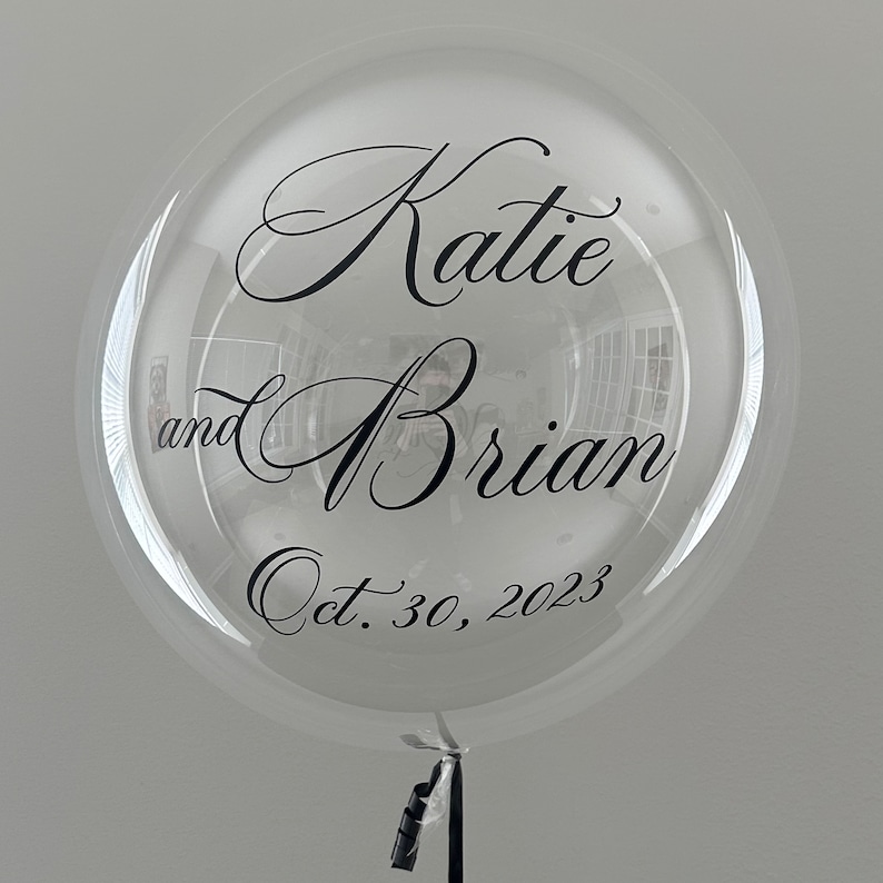 May include: Clear balloon with black lettering that reads "Katie and Brian Oct. 30, 2023".