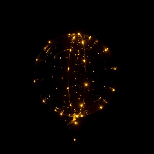 Puede incluir: Un globo transparente con luces LED blancas c&aacute;lidas enroscadas a su alrededor. El globo est&aacute; inflado y parece flotar en una habitaci&oacute;n oscura.
