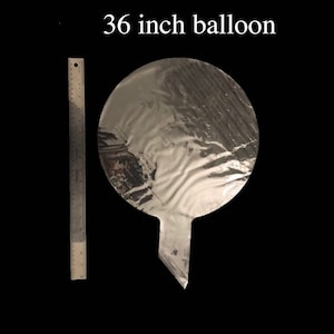 May include: A silver 36 inch balloon, deflated, with a long, pointed tail. A ruler is next to the balloon for size comparison.