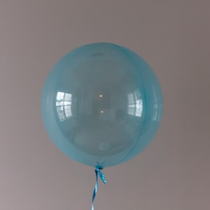 May include: A light blue balloon with a blue ribbon tied to the bottom. The balloon is inflated and appears to be transparent, reflecting the surrounding environment.