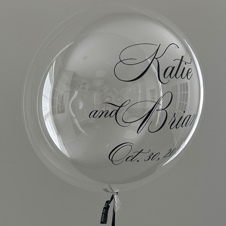 May include: A clear bubble balloon with black lettering that reads "Katie and Brian Oct. 30, 20..."