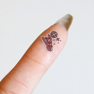 May include: A finger with a small sticker of a person skiing with a disco ball and stars.