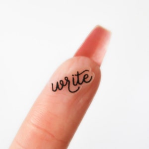 May include: A finger with a clear sticker that says "write" on it.