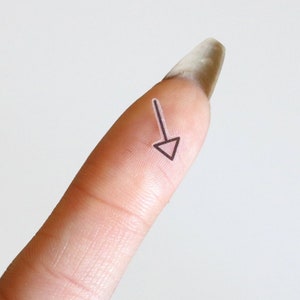 May include: A close-up of a finger with a small black arrow drawn on it.