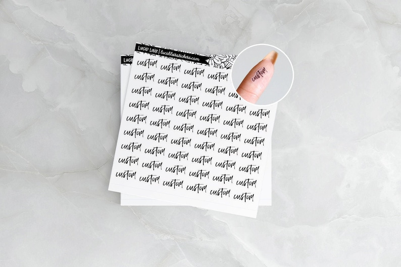 May include: White sticker sheets with the word "custom" printed in a handwritten style, repeated across the surface. A close-up shows the word "custom" as a temporary tattoo on a finger. The stickers have the Lucid Lane logo.