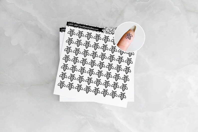 Op de afbeelding: Een vel wit papier met een raster van zwarte bijenstickers. De bijenstickers zijn klein en eenvoudig, met een zwarte omtrek en een gestreept lichaam.