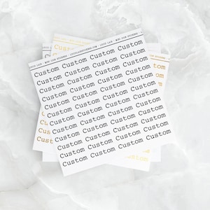 May include: Several sheets of white stickers with the word "Custom" printed repeatedly in black. Some sheets have gold lettering. The stickers are from Lucid Lain Mini Icon Stickers.