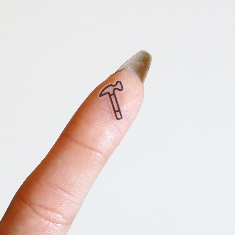 May include: A finger with a clear sticker of a hammer on it.
