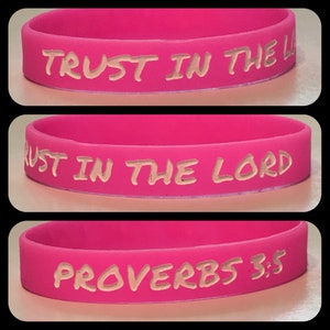 May include: Pink silicone wristband with the text "TRUST IN THE LORD" and "PROVERBS 3:5" in white lettering.