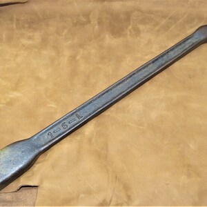 May include: A long, black metal tool with a rounded handle and a flat, rectangular head. The tool is marked with the text "1-6-L".