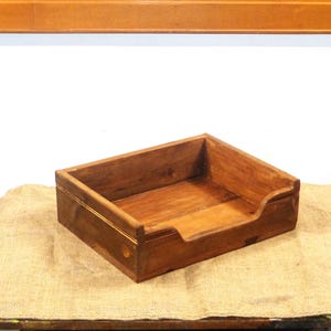May include: A rectangular wooden tray with a dark brown finish. The tray has a cutout on one side and a gold accent. The tray is sitting on a burlap surface.