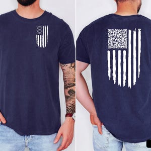 May include: Navy blue t-shirt featuring a distressed white American flag design on the front and back. The front has a small flag, while the back has a larger flag with a QR code. The shirt is a comfortable, casual style.