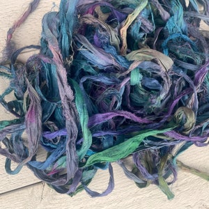 K&ouml;nnte beinhalten: Ein Haufen von teal-, lila- und blauen Seidenbandresten. Das Band ist handgef&auml;rbt und hat eine leicht ausgefranste Textur.