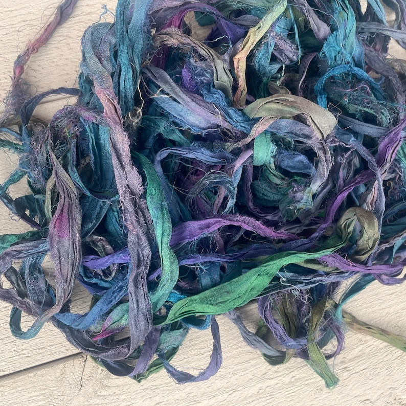 K&ouml;nnte beinhalten: Ein Haufen von teal-, lila- und blauen Seidenbandresten. Das Band ist handgef&auml;rbt und hat eine leicht ausgefranste Textur.