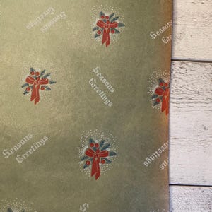 May include: Green wrapping paper with a repeating pattern of red bows with green holly and berries. The text "Seasons Greetings" is printed in black on the paper.