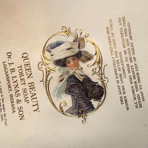 May include: A vintage advertisement for Queen Beauty Toilet Soap, featuring a woman in a hat and a floral bouquet. The text reads "Queen Beauty Toilet Soap, Dr. J. B. Lynas & Son, Logansport, Indiana".