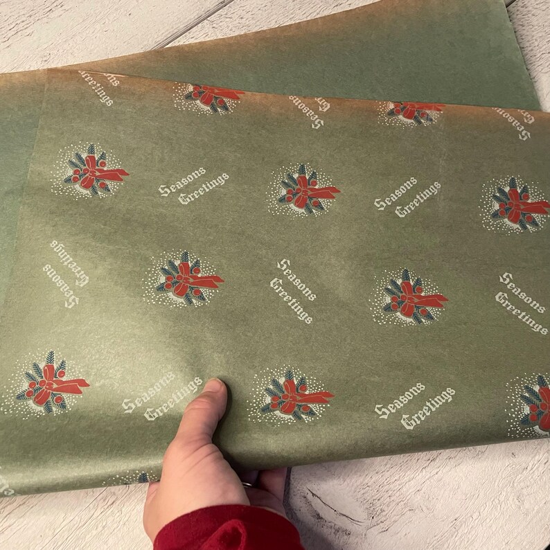 May include: Green wrapping paper with a repeating pattern of red and green holly sprigs with a red bow and the text "Seasons Greetings".