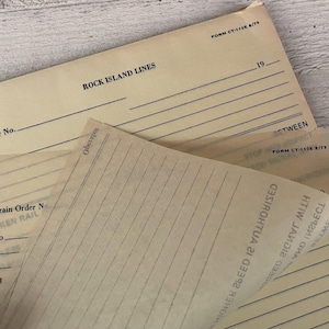 May include: A stack of vintage Rock Island Lines train order forms printed on light tan paper. The forms feature black text, including 'FORM CT-110E 8/73', 'Train Order No.', and 'Operator'. The translucent top sheet shows printed lines and text.