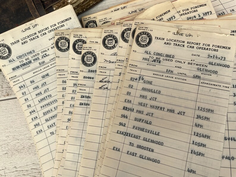 May include: A stack of vintage train location report forms for foremen and track car operators. The forms are printed on white paper with black ink and have a "Safety First" logo. The forms are dated September 1, 1973 and September 14, 1973. The forms list train numbers, locations, and times.