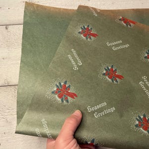 May include: Green wrapping paper with a repeating pattern of red and green wreaths with a bow and the text "Seasons Greetings".