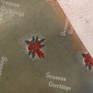 May include: Green wrapping paper with a repeating pattern of red bows and sprigs of pine with red berries. The paper has the text "Seasons Greetings" printed in white.