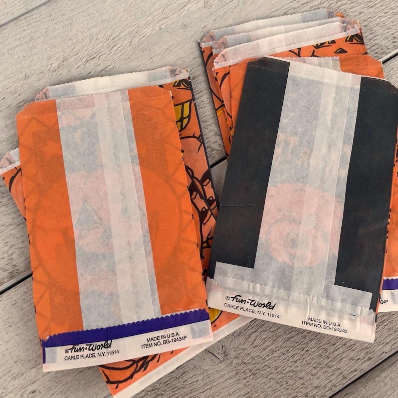 May include: A stack of orange and black Halloween treat bags with a white stripe down the center. The bags have a cartoon image of a jack-o-lantern on them. The bags are labeled "Fun-World" and have the text "Made in U.S.A. Item No. BG-19434P".