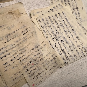 Może przedstawiać: Kolekcja postarzanych, kremowych arkuszy papieru z odręcznym tekstem czarnym tuszem. Pismo wydaje się być w języku azjatyckim, prawdopodobnie japońskim. Papier ma zużyty, zabytkowy wygląd, sugerujący wiek i znaczenie historyczne.