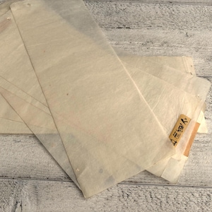 May include: A stack of rectangular, translucent paper sheets, possibly for wrapping or packaging. The paper is off-white with subtle variations in tone. A small, rectangular label with Japanese text is visible on one of the sheets.