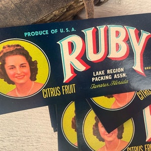 Op de afbeelding: Vintage citrusfruit-etiket met een portret van een vrouw, de tekst "RUBY" in rode en blauwe letters en de woorden "PRODUCE OF U.S.A." en "CITRUS FRUIT".