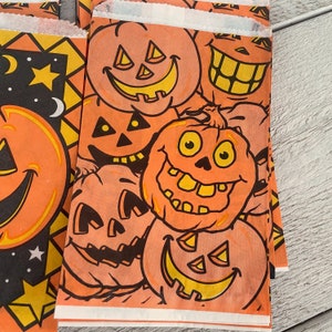 May include: Orange and black Halloween themed gift bags with various jack-o'-lantern faces printed on them. The bags are made of paper and have a festive design.