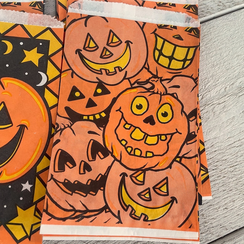 May include: Orange and black Halloween themed gift bags with various jack-o'-lantern faces printed on them. The bags are made of paper and have a festive design.