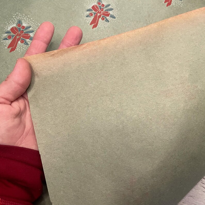 May include: A sheet of green wrapping paper with a repeating pattern of red bows and green wreaths. The paper is slightly wrinkled and has a vintage look.