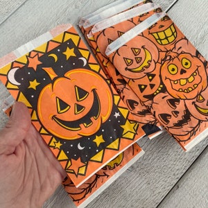 May include: Orange and black Halloween treat bags with a variety of jack-o'-lantern designs. The bags feature stars, moons, and the words "Happy Halloween".
