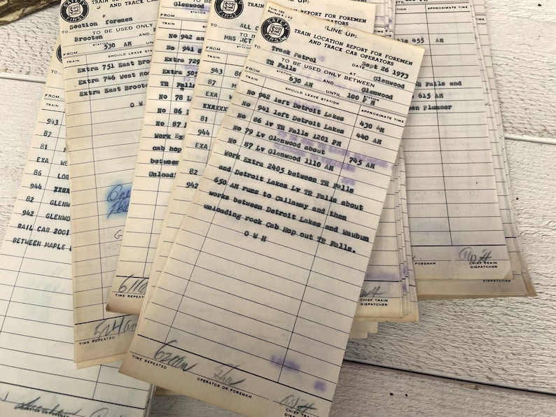 May include: A stack of vintage train location report forms for foremen and trace car operators. The forms are printed on white paper with blue ink and have a date of June 26, 1973. The forms list train numbers, locations, and approximate times.