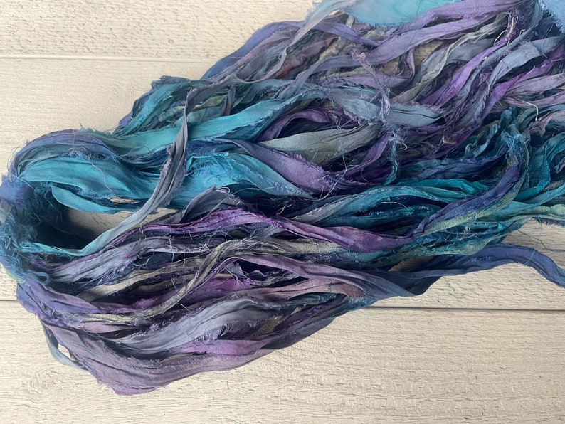 K&ouml;nnte beinhalten: Ein B&uuml;ndel aus t&uuml;rkisfarbenem, blauem und violettem Seidenband. Das Band ist ausgefranst und hat einen rustikalen, handgefertigten Look.