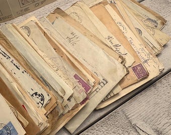 May include: A collection of vintage envelopes, varying in size and color, with stamps and handwritten text. The envelopes are arranged in a pile, showcasing their aged appearance. Some envelopes have purple stamps and blue stamps.