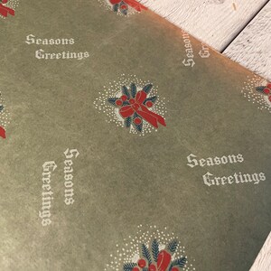 May include: Green wrapping paper with a repeating pattern of red bows and holly sprigs. The paper also has the text "Seasons Greetings" printed in white.