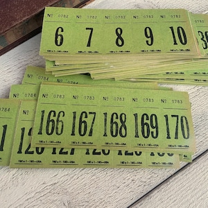 Puede incluir: Una pila de boletos verdes vintage con numeración negra, que van del 6 al 10 y del 166 al 170. Cada boleto tiene el número "0782" o "0783" impreso en la parte superior. Los boletos están sobre una superficie de madera blanca.