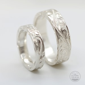 May include: Two silver rings with intricate floral designs. The rings are engraved with a pattern of leaves and flowers. The rings are a popular choice for wedding bands.