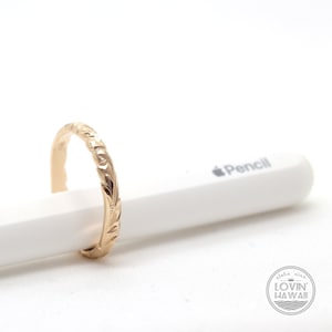 Puede incluir: Un anillo de banda de oro con un dise&ntilde;o floral. El anillo est&aacute; sobre una superficie blanca.