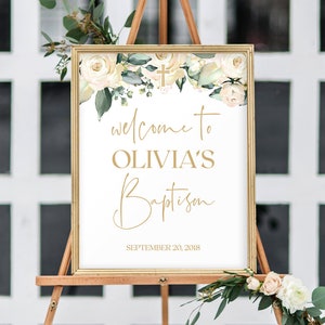 May include: A white sign with gold lettering announcing "Welcome to Olivia's Baptism" with a floral design and a gold cross at the top. The date "September 20, 2018" is printed at the bottom.