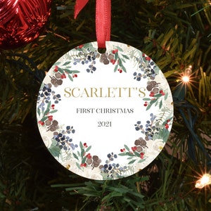 May include: A white round Christmas bauble with a gold wreath design and the text "SCARLETT'S FIRST CHRISTMAS 2021".