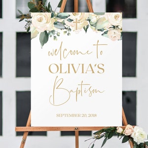 May include: White sign with gold lettering announcing "Welcome to Olivia's Baptism" with a floral border and a gold cross. The date "September 20, 2018" is printed below the text.